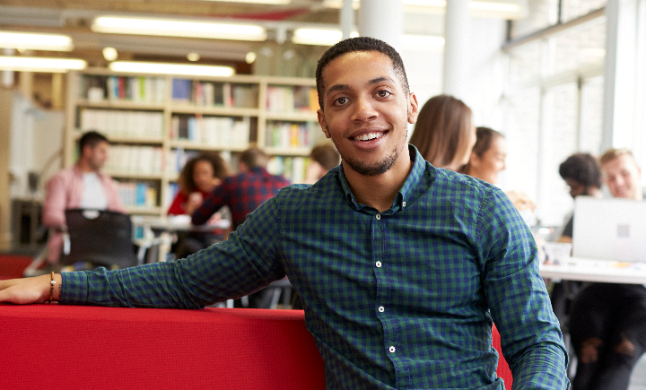 student sitting, smiling on a couch in a university library